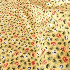 May include: Yellow fabric with a repeating pattern of small red, white, and blue flowers. The fabric is textured and has a slightly wrinkled appearance.