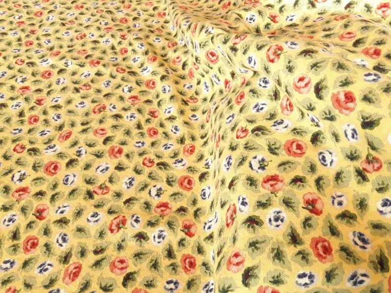 May include: Yellow fabric with a repeating pattern of small red, white, and blue flowers. The fabric is textured and has a slightly wrinkled appearance.