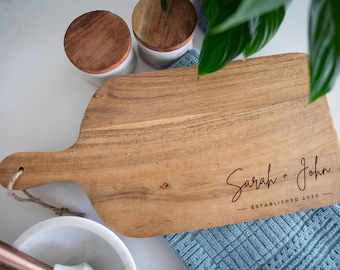 May include: A wooden cutting board with a handle, engraved with the text "Sarah + John - Established 2020".