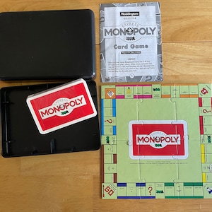 Könnte beinhalten: Eine rote und weiße Spielkartenbox mit der Aufschrift "Express Monopoly" auf der Vorderseite. Die Box ist geöffnet und die Spielteile sind sichtbar. Das Spielbrett ist grün und hat ein rotes und weißes "Express Monopoly"-Logo in der Mitte. Das Spiel enthält ein Kartenspiel und eine Spielanleitung.