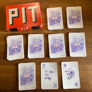 Könnte beinhalten: Ein Vintage-Brettspiel namens "PIT" mit einer roten Box und Karten. Die Karten zeigen Illustrationen von Menschen und Rohstoffen wie Mais, Gerste und Weizen. Das Spiel ist für mehrere Spieler konzipiert.
