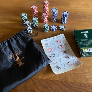 Könnte beinhalten: Ein Pokerset mit verschiedenfarbigen Chips, einem schwarzen Kordelzugbeutel mit dem Aufdruck "Waddingtons Number 1", einer Poker-Rangliste und einer grünen Kartenbox.