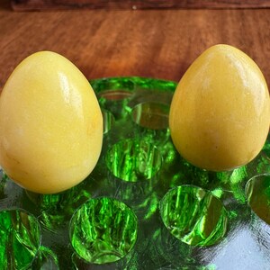 May include: Two yellow marble eggs sitting in a green glass egg holder.