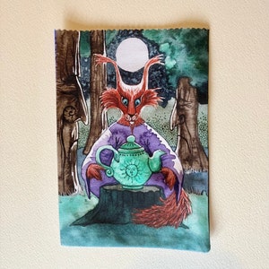 May include: A watercolor painting of a red fox wearing a purple robe and holding a green teapot with a sun design. The fox is sitting on a tree stump in a forest setting with a full moon in the background.