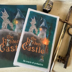 May include: Two copies of "The Hidden Castle" book with a castle and dragon illustration. A sword, key, and helmet are next to the books. The book cover has the text "The Hidden Castle" and "An oracle of protection".