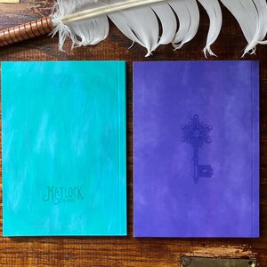 May include: Two hardcover journals. One is teal with the text "Matlock the Hare" embossed on the cover. The other is purple with an embossed key design. A feather quill rests above the journals.