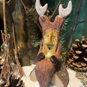 May include: A ceramic figurine of a woodland creature with antlers, a brown body, and a yellow face. The figurine is sitting on a wooden log.