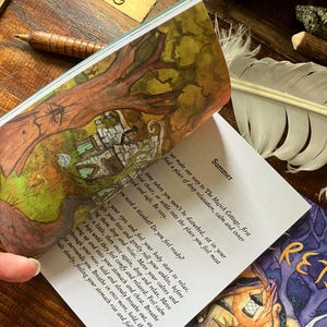 May include: An open book with colorful illustrations and text, featuring a tree and a cottage scene. The page reads "Summer" and includes instructions for relaxation. A wooden pen and a feather are also visible.