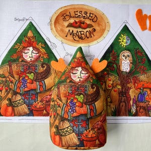 May include: A fabric craft panel featuring a Blessed Mabon design with a central figure holding a cornucopia, surrounded by autumn imagery like pumpkins, an owl, and a sun. The panel includes cut-out shapes and a stuffed figure with orange felt ears.