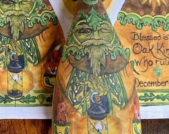 May include: A cone-shaped fabric ornament featuring a printed illustration of a bearded green figure with oak leaves, a lantern, a squirrel, and a fox. The design includes warm yellow, brown, and green tones with an acorn motif at the top point.