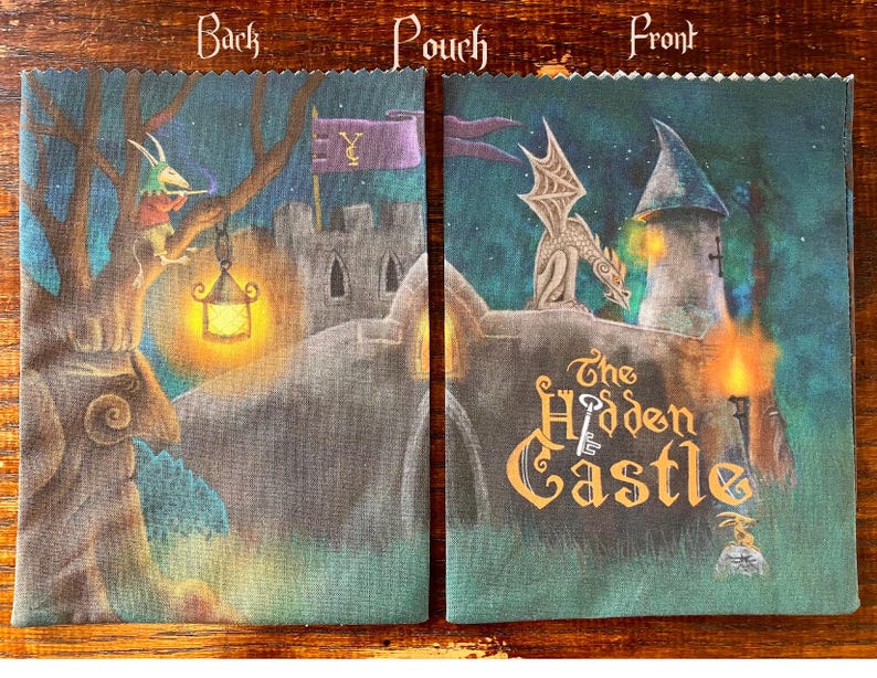 May include: A fabric pouch with a fantasy castle scene. The front features a dragon on a tower and the words "The Hidden Castle." The back shows a tree with a figure and a lantern. The pouch is in shades of blue, green, and brown.
