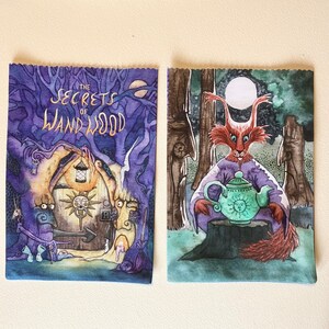 May include: Two book covers with watercolor illustrations. The first cover is purple with a gold title "The Secrets of Wandwood". The second cover is blue with a red fox holding a green teapot with a yellow sun face.