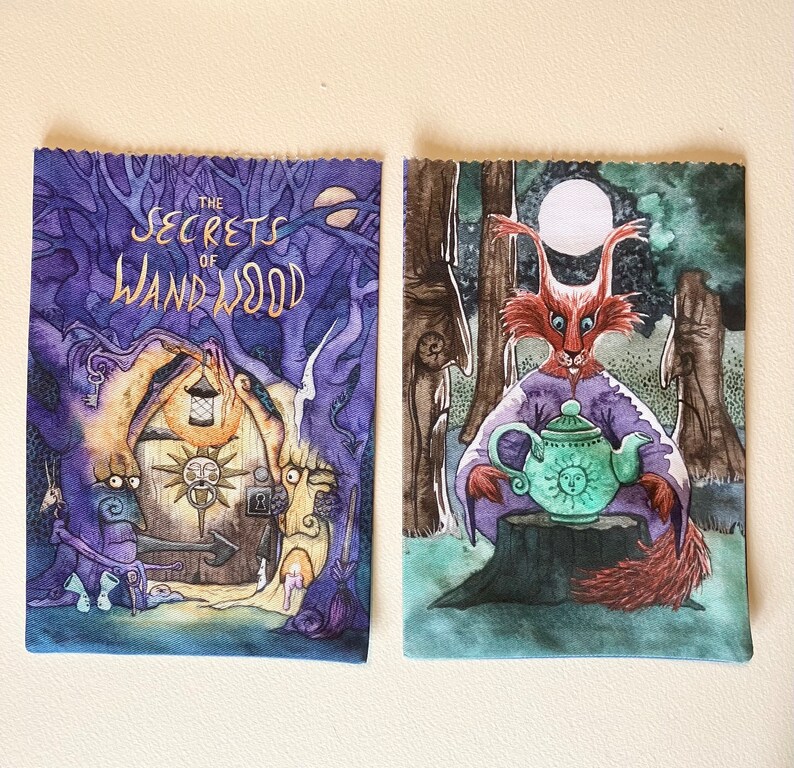 May include: Two book covers with watercolor illustrations. The first cover is purple with a gold title "The Secrets of Wandwood". The second cover is blue with a red fox holding a green teapot with a yellow sun face.