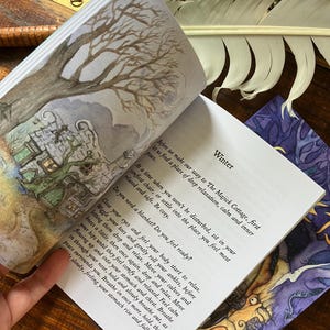 May include: Open book with watercolor illustrations and text. The left page features a drawing of a tree and a cottage. The right page has the word "Winter" and instructions for relaxation. A feather and other items are in the background.