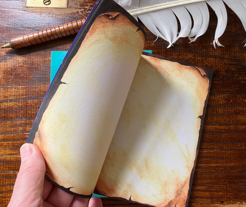 May include: A notebook with pages designed to look like aged parchment. The edges of the pages are darkened, giving the appearance of an antique document. A wooden pen and a feather are also visible.