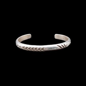 May include: A silver cuff bracelet featuring a polished metallic finish with engraved decorative patterns. The design includes a series of small circular indentations, a repeating leaf-like motif, and a sunburst-style engraving along the band.