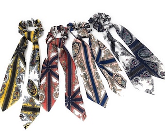 May include: Five colorful hair scrunchies with long, patterned fabric tails. The scrunchies are in shades of yellow, red, blue, pink, and white with paisley and floral designs.