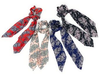 May include: Four hair scrunchies with paisley patterns in red, pink, black, and blue. The scrunchies are made of soft fabric and have a comfortable fit.