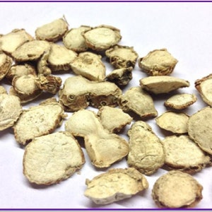 May include: Dried ginger root slices, light brown in colour, with a rough texture. The slices are arranged on a white surface.