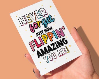 May include: A white card with colorful text that reads "Never forget just how FLIPPIN' AMAZING YOU ARE". The card is held in a hand against a peach background.