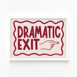 May include: A white framed print with a red wavy border. The print features the text "Dramatic Exit" in red with a red hand pointing to the right.