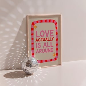 May include: A framed print with a pink and white striped border and the text "LOVE ACTUALLY IS ALL AROUND" in pink and orange letters.