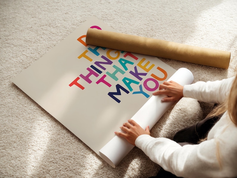 May include: A person unrolling a poster with the text "Do the things that make you happy" in colorful letters. The poster is on a white background.