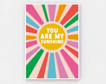 May include: A colorful sunburst design with the text "You are my sunshine" in a yellow circle in the center. The background is a light pink color.