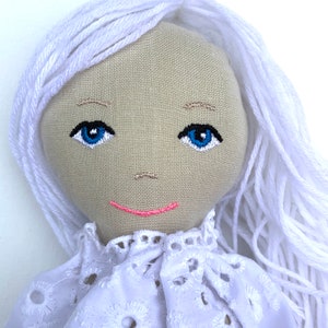 May include: A handmade doll with white yarn hair, a white lace collar, and an embroidered face with blue eyes and a pink smile.