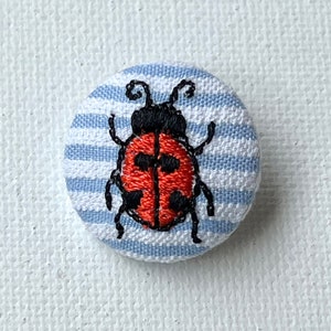 Op de afbeelding: Een knoop van blauw-wit gestreept stof met een geborduurde rode en zwarte lieveheersbeestje.