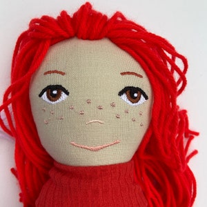 May include: Handmade doll with red yarn hair, embroidered facial features, and a red sweater.
