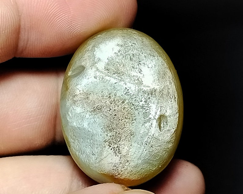 May include: A smooth, oval-shaped, light green and gold gemstone with a mottled pattern.