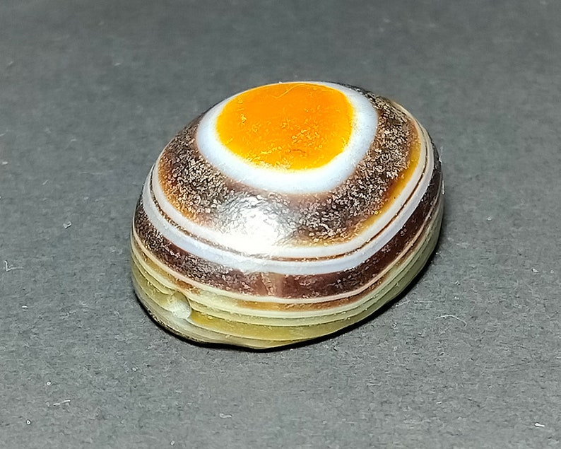 May include: A banded agate stone with a white and orange center, surrounded by brown and white bands.