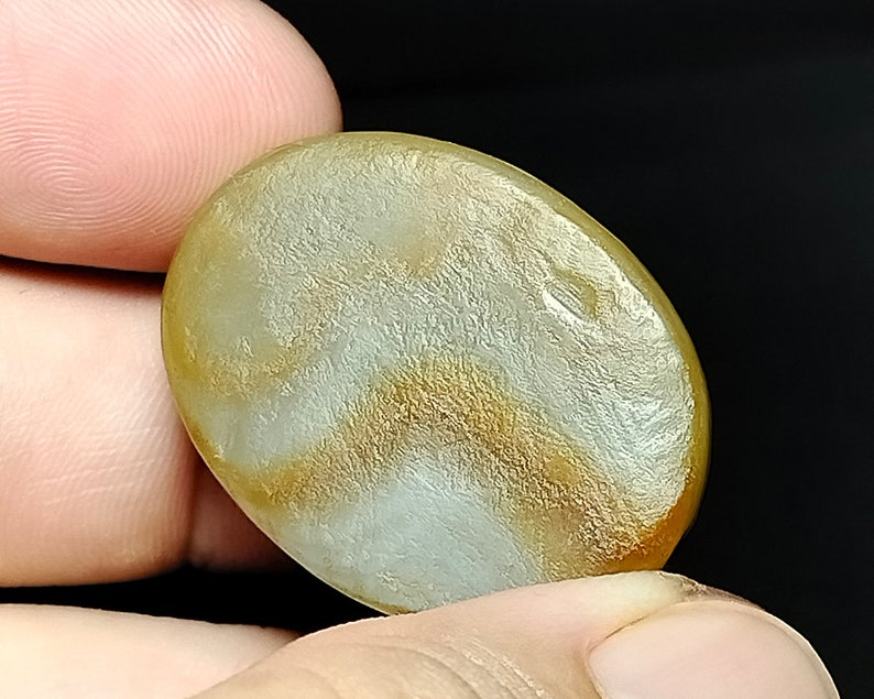 May include: A smooth, oval-shaped, light brown agate gemstone with white and gold swirling patterns.