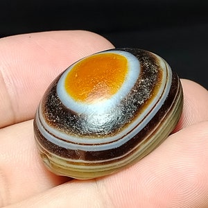 May include: A banded agate stone with a large orange center and multiple brown and white bands.