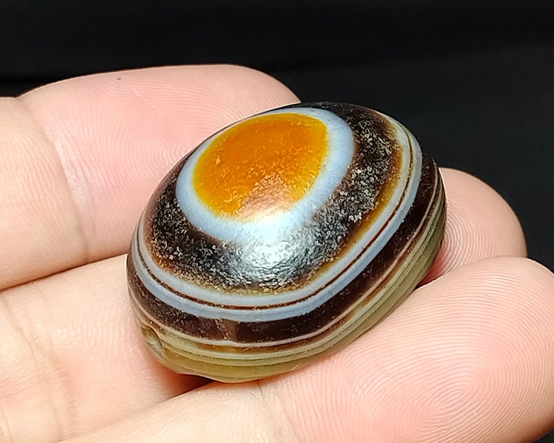 May include: A banded agate stone with a large orange center and multiple brown and white bands.