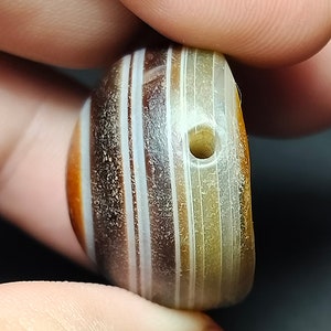 May include: A round, striped agate bead with a hole drilled through the center. The bead is a mix of brown, white, and cream colors.