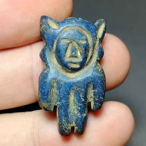 Könnte beinhalten: Eine kleine, blaue, geschnitzte Figur eines Menschen mit einem stilisierten Gesicht. Die Figur ist aus einem harten, glatten Material gefertigt und hat eine leicht abgenutzte Optik.