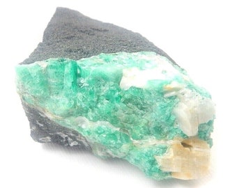 May include: A rough piece of dark gray rock with a cluster of bright green emeralds embedded in it. The emeralds are surrounded by white and light brown crystals.