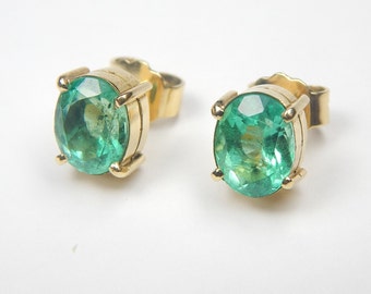 May include: A pair of gold earrings with emerald green gemstones. The earrings have a simple, classic design.