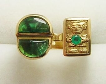 May include: A gold ring featuring two green gemstones. The larger gemstone is a semi-circular shape and the smaller gemstone is square.