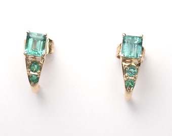 May include: A pair of gold earrings with a rectangular, light blue-green gemstone at the top and three smaller, round, green gemstones below. The earrings are set against a white background.