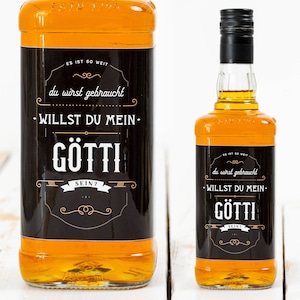 Könnte beinhalten: Zwei Flaschen mit bernsteinfarbener Flüssigkeit und schwarzen Etiketten. Die Etiketten haben weißen Text, der "ES IST SO WEIT du wirst gebraucht -WILLST DU MEIN- GÖTTI SEIN?" und "du wirst gebraucht -WILLST DU MEIN- GÖTTI SEIN?" lautet.