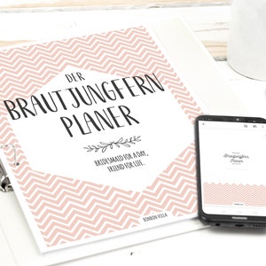 Könnte beinhalten: Ein rosa-weißer Hefter mit Chevron-Muster und dem Text "Der Brautjungfern Planer" sowie dem Spruch "Bridesmaid for a day, friend for life." Der Hefter ist geöffnet und zeigt eine Seite mit dem gleichen Chevron-Muster. Ein Smartphone mit einem ähnlichen Chevron-Muster liegt auf dem Hefter.