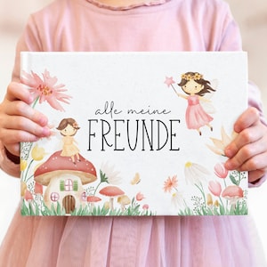 Könnte beinhalten: Ein weißes Buch mit einer Aquarell-Illustration einer Fee und einem Pilzhaus. Das Buch trägt den Text "alle meine FREUNDE" auf der Vorderseite.
