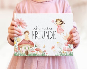 May include: A white book with a watercolor illustration of a fairy and a mushroom house. The book has the text "alle meine FREUNDE" on the front.