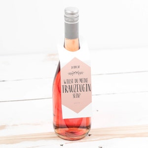 Puede incluir: Una botella de vino rosado con una etiqueta blanca que dice "Willst du meine Trauzeugin sein?" que se traduce como "¿Quieres ser mi dama de honor?" en español.