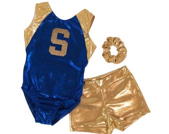 May include: A blue and gold gymnastics leotard with a gold letter "S" on the front. The leotard is paired with gold shorts and a gold hair scrunchie.