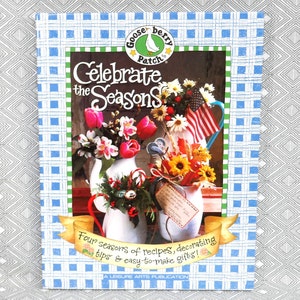 May include: A book titled "Celebrate the Seasons" with a blue and white checkered cover. The cover features a floral arrangement with a gooseberry patch logo. The book includes recipes, decorating tips, and easy-to-make gift ideas.