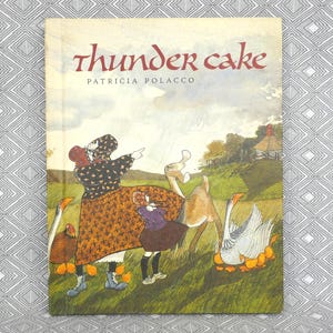 以下が含まれることがあります： パトリシア・ポラッコ著「サンダーケーキ」の表紙。イラストは、女性と子供が野原の鹿とガチョウを指している様子を描いています。タイトルは赤い筆記体で書かれています。